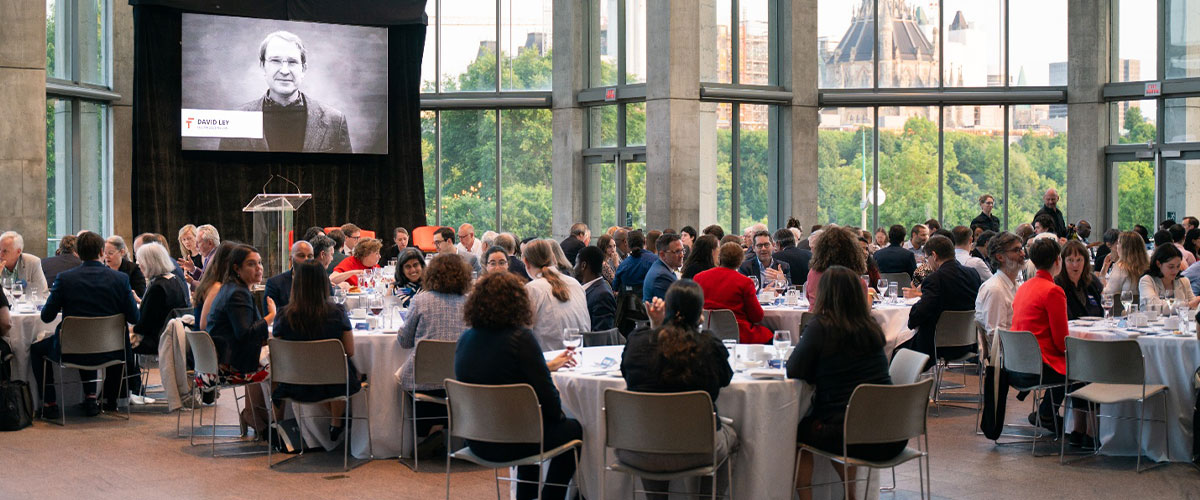 Plusieurs personnes assisent à des tables et qui discutent avant une conférence.
